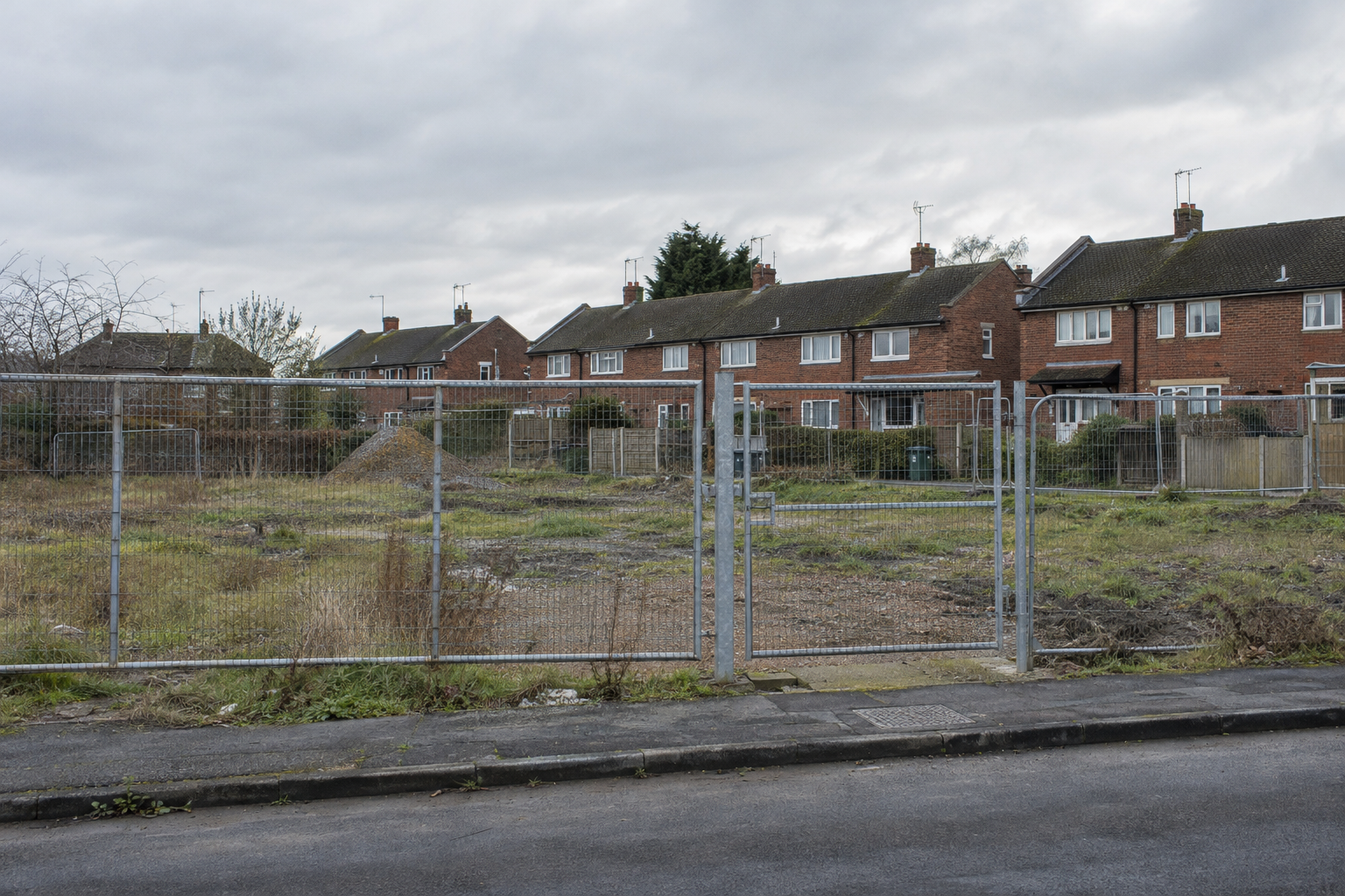 Fenced undeveloped land beside red-brick homes in England, illustrating the Council Housebuilding Support Fund